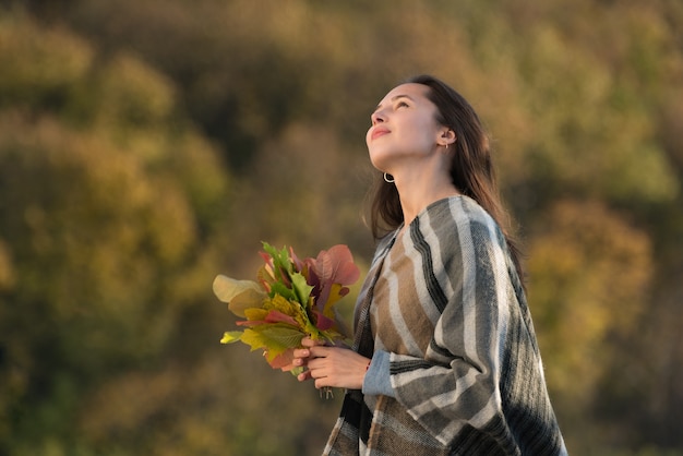 Jeune femme dans un poncho avec un bouquet de feuilles d'automne