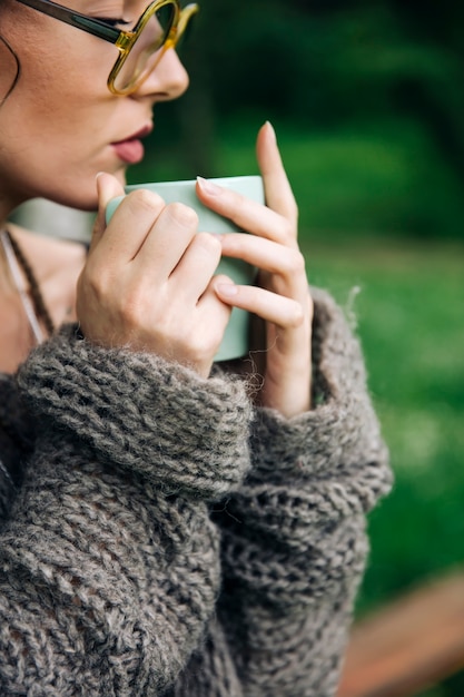 Jeune femme, dans, a, pull, et, à, lunettes, boire café, dans parc