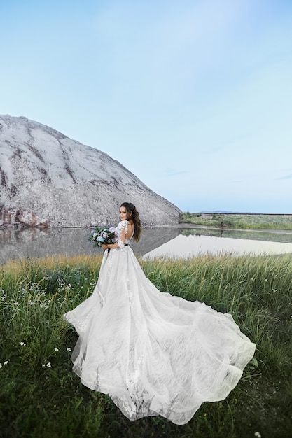 Jeune femme dans une robe de mariée tenant le bouquet de mariée et posant dans un beau paysage.