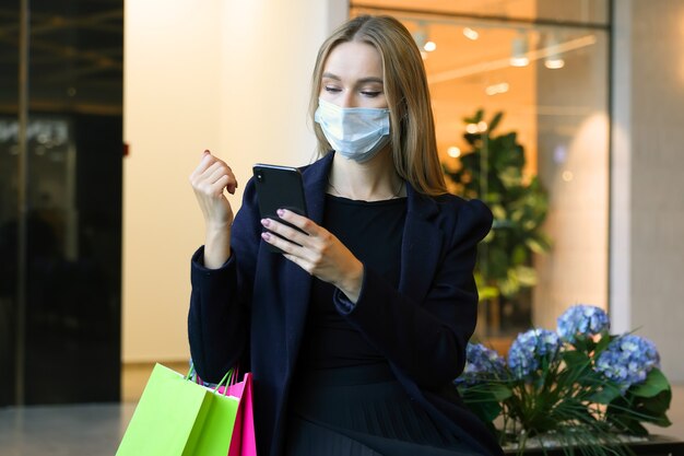 Une jeune femme dans un type de masque de protection sur son téléphone après le shopping