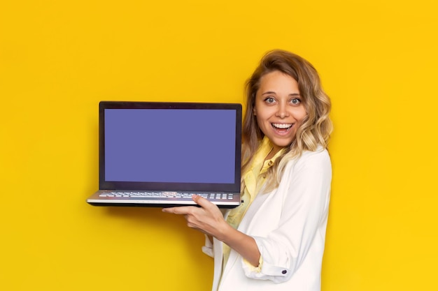 Une jeune femme dans une veste blanche montre un écran d'ordinateur portable très vierge pour le texte ou la conception