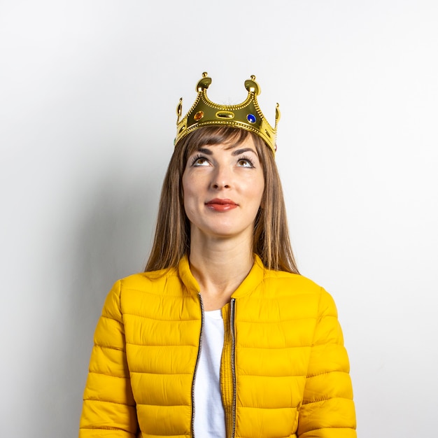 Jeune femme dans une veste jaune et une couronne en or sur fond clair.