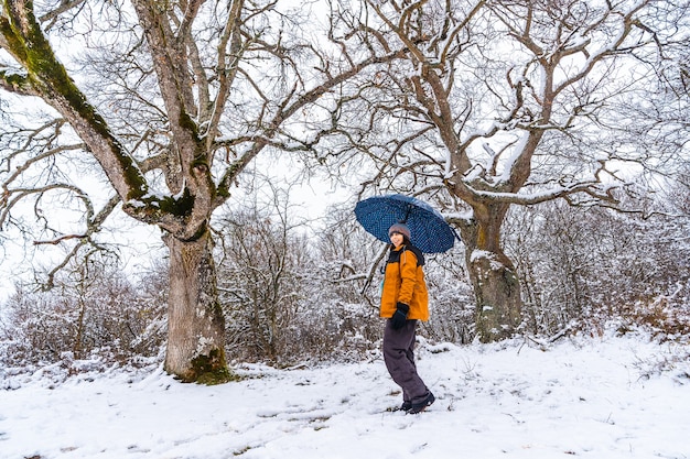 Une jeune femme dans une veste jaune et un parapluie jouant avec la neige sur une branche d'arbre. Neige dans la ville d'Opakua près de Vitoria