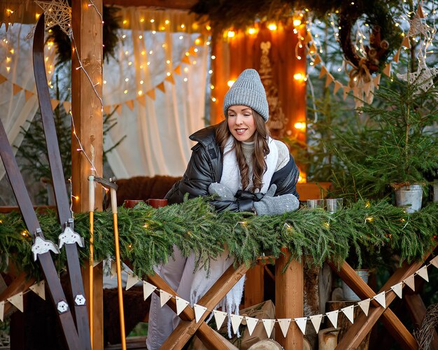 Une jeune femme dans une veste noire et un pantalon blanc dans un gazebo de Noël de style scandinave