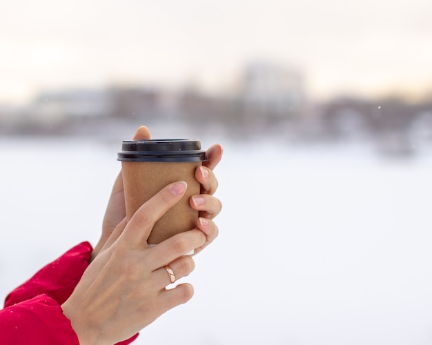 Une jeune femme dans une veste rouge en hiver tient un verre de café ou de thé chaud