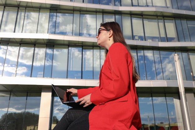 Jeune femme dans une veste travaillant avec un ordinateur portable dans le contexte d'un immeuble de bureaux