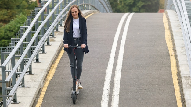 Une jeune femme dans des vêtements élégants monte un scooter électrique sur une piste cyclable