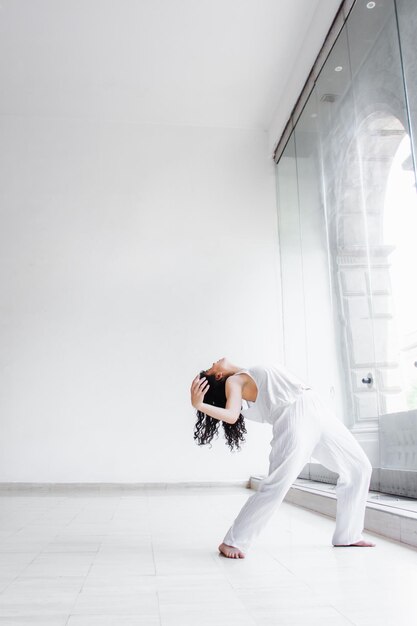 Jeune femme dansant dans un studio lumineux blanc