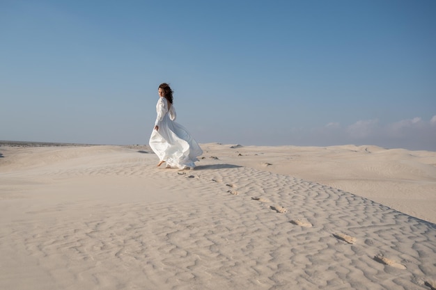 Jeune femme dansant en robe de mariée blanche sur une dune de sable dans le désert