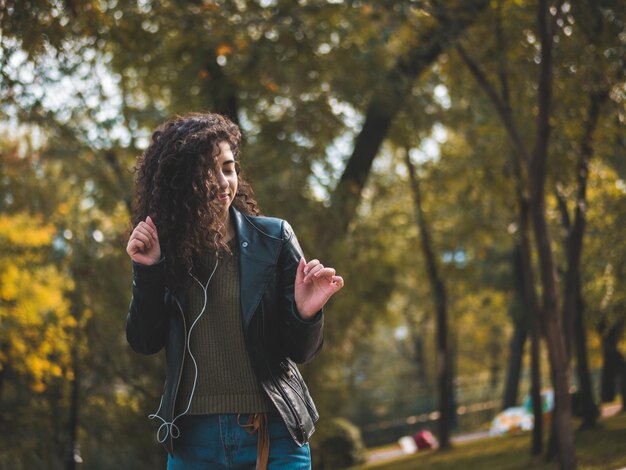 Photo une jeune femme danse sur de la musique contre des arbres dans un parc.