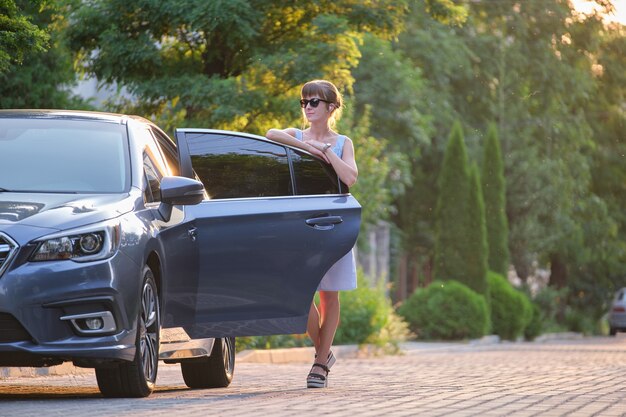 Jeune femme debout à côté de sa voiture en attente de quelqu'un. Concept de voyage et de vacances.