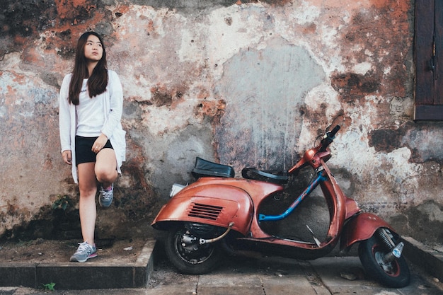 Une jeune femme debout à côté d'un scooter contre le mur