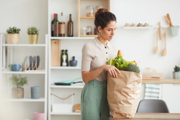 Jeune femme debout dans la cuisine et acheter la nourriture dans un sac en papier