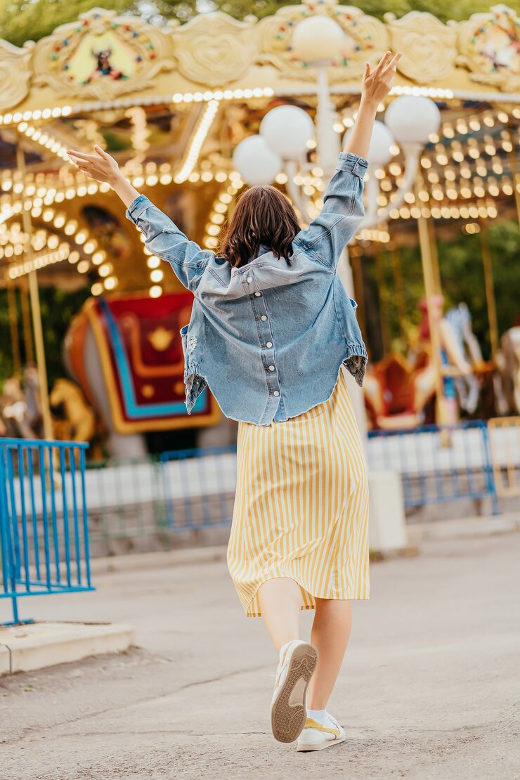 Photo jeune femme debout devant le carrousel avec éclairage nocturne au parc d'attractions. vue arrière