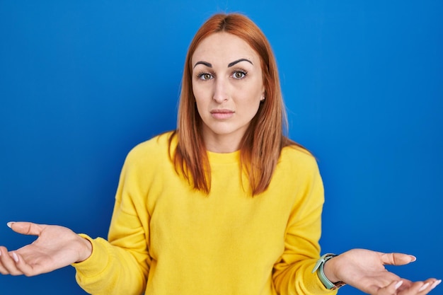 Jeune femme debout sur fond bleu désemparé et confus avec les bras ouverts aucune idée de concept