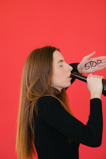 Jeune femme debout sur fond rouge et tenant une bouteille de vin Arrêter l'alcool