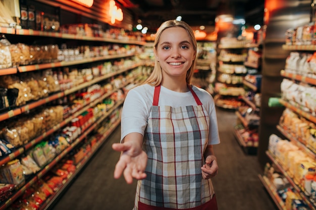 Jeune femme debout en ligne entre deux étagères de pâtes en épicerie.