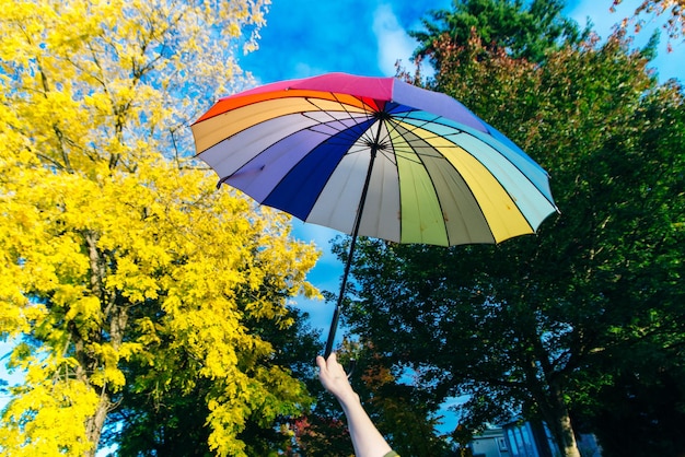 Jeune femme debout avec un parapluie multicolore et le tourne contre avec un ciel bleu