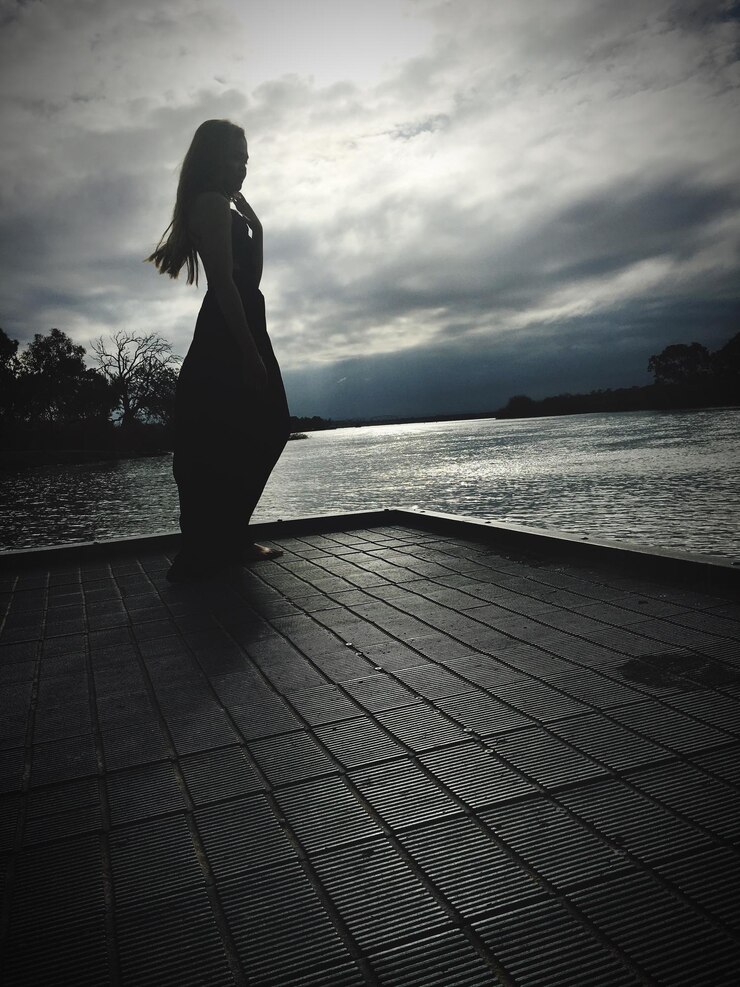 Photo une jeune femme debout sur la promenade près de la rivière contre un ciel nuageux