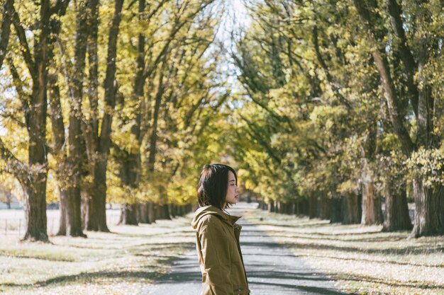 Une jeune femme debout sur la route contre des arbres dans le parc pendant une journée ensoleillée