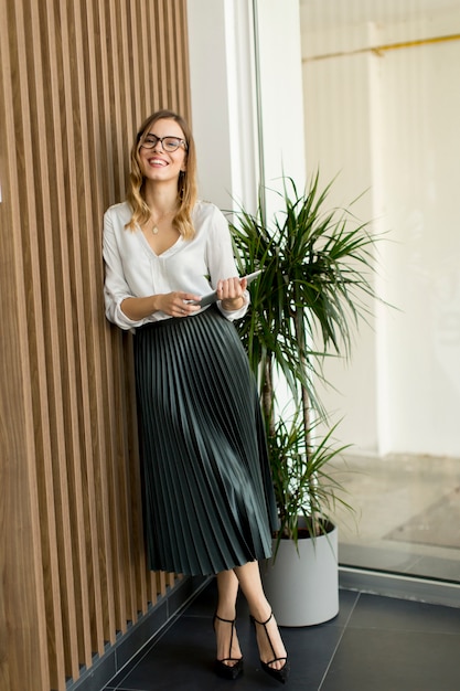 Jeune femme debout avec tablette par mur au bureau