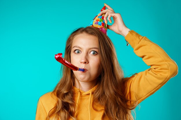 Jeune femme décontractée en cône de fête avec corne sur fond bleu