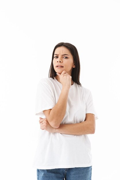 Jeune femme décontractée pensive debout isolée sur un mur blanc