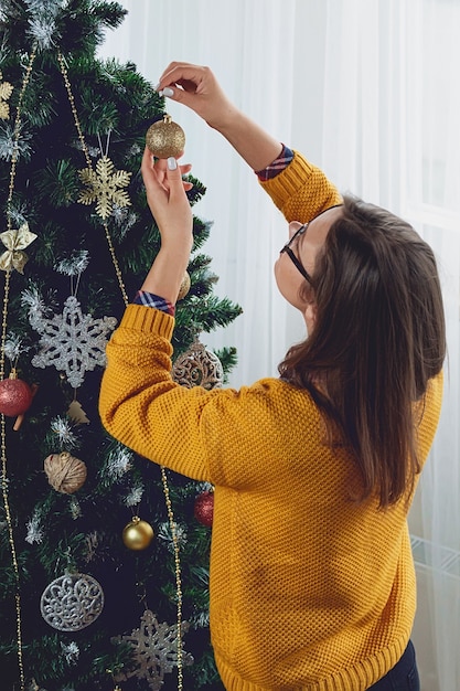 Jeune femme décore l'arbre de Noël, tient le ballon d'or
