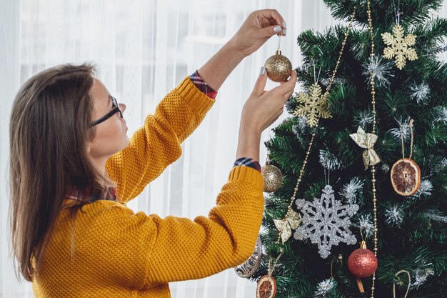 Jeune femme décore l'arbre de Noël, tient le ballon d'or