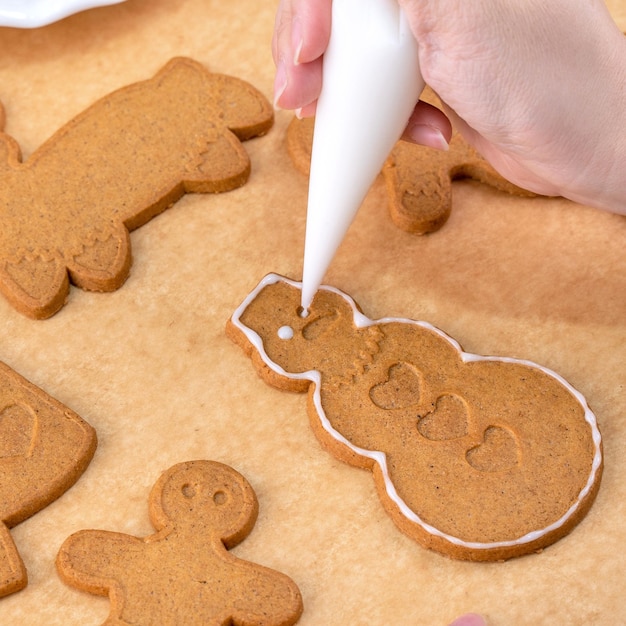 Photo jeune femme décore noël gingerbread house cookies biscuit à la maison avec garniture de glaçage dans un sac de glaçage close up lifestyle