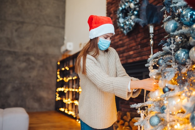 Une jeune femme décore le sapin de Noël dans des masques médicaux