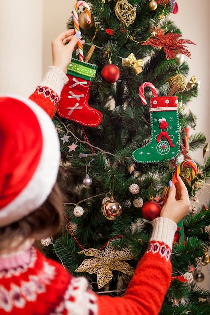 Jeune femme décorer un arbre de Noël avec des cannes de bonbon à la maison, portant bonnet de Noel.