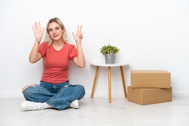 Jeune femme déménageant dans une nouvelle maison parmi des boîtes isolées sur fond blanc comptant huit avec les doigts