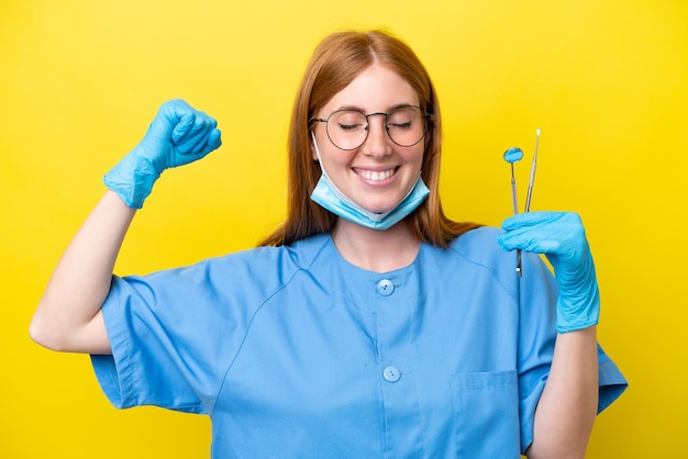 Jeune femme dentiste rousse isolée sur fond jaune faisant un geste fort