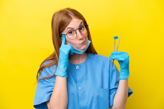 Jeune femme dentiste rousse isolée sur fond jaune en pensant à une idée