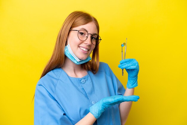 Jeune femme dentiste rousse isolée sur fond jaune tendant les mains sur le côté pour inviter à venir