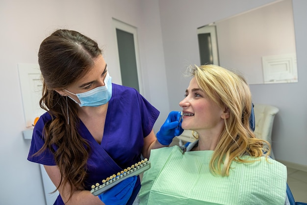 jeune femme dentiste spécialisée dans des vêtements spéciaux montre une palette de couleurs de dents pour une patiente. Concept de blanchiment des dents