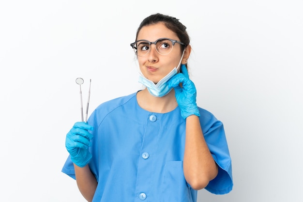 Jeune femme dentiste tenant des outils isolés sur fond blanc ayant des doutes