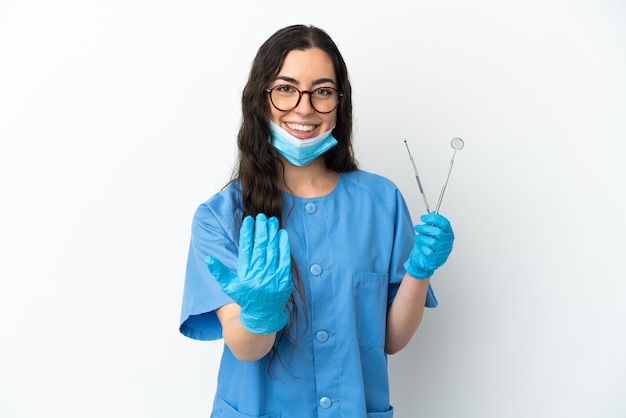 Jeune femme dentiste tenant des outils isolés sur fond blanc invitant à venir avec la main. Heureux que tu sois venu