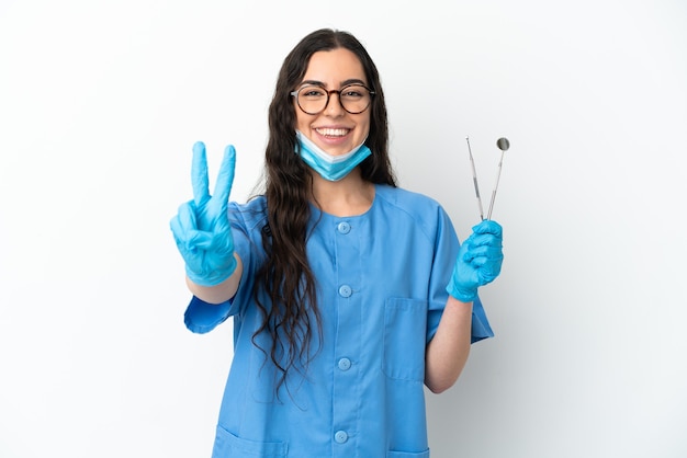 Jeune femme dentiste tenant des outils isolés sur fond blanc souriant et montrant le signe de la victoire