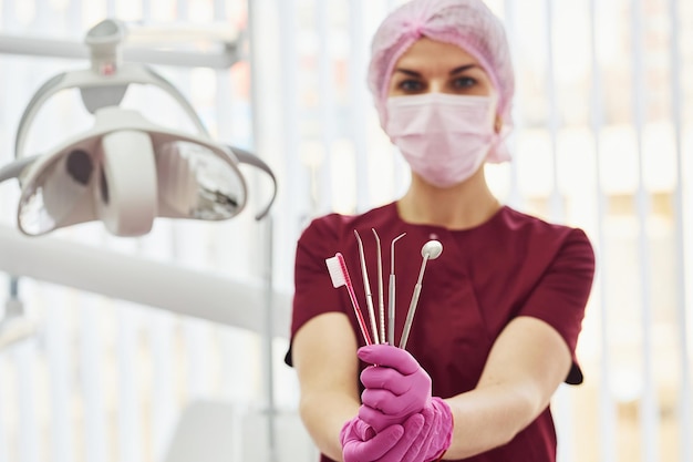 Jeune femme dentiste en uniforme debout dans le bureau de stomatologie tenant une brosse et des outils