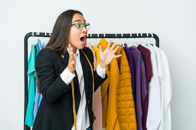 Jeune femme de designer asiatique isolée sur fond blanc crie fort, garde les yeux ouverts et les mains tendues.