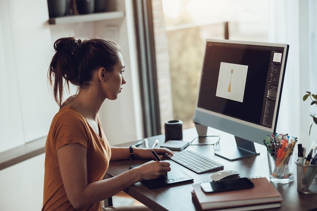 Jeune femme designer travaillant sur ordinateur depuis son bureau à domicile.