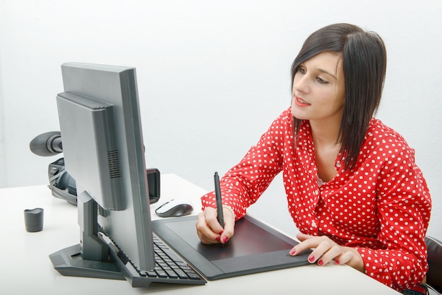 Jeune femme designer utilisant une tablette graphique tout en travaillant avec un ordinateur