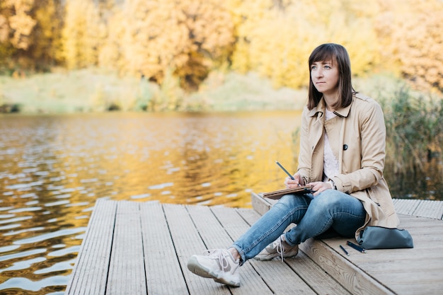 Jeune femme dessinant près d'un lac dans la forêt d'automne