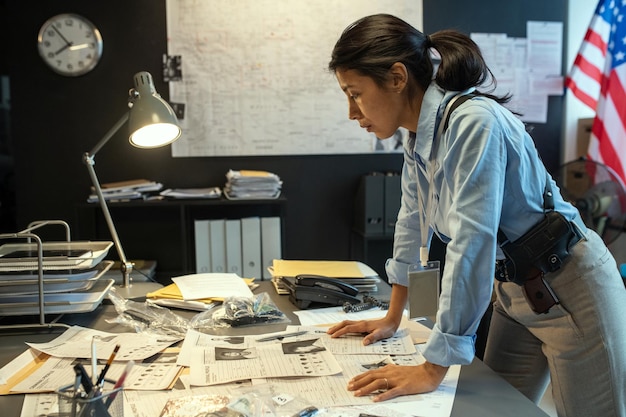 Jeune femme détective sérieuse en uniforme se penchant sur le bureau avec des documents