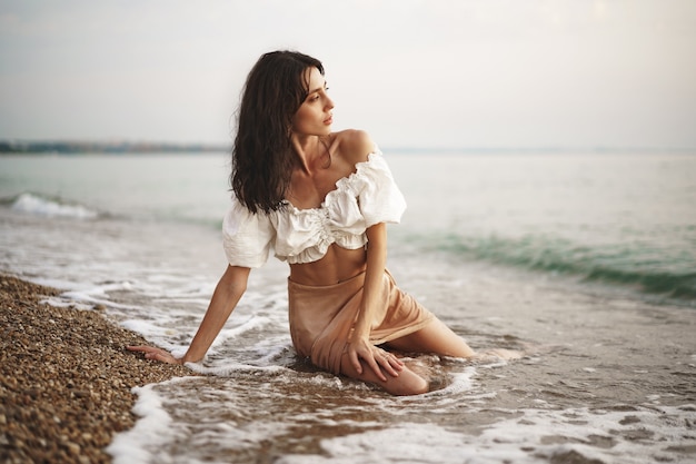 Jeune femme détendue assise toute seule sur une plage vide