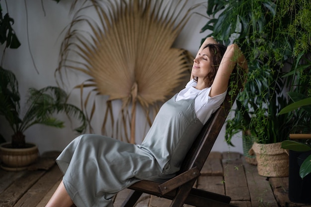 Jeune femme détendue s'asseoir sur un fauteuil confortable dans un élégant jardin intérieur avec des plantes exotiques vertes