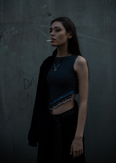 Photo une jeune femme détournant les yeux pendant qu'elle fume debout contre le mur.