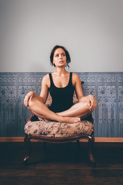 Photo une jeune femme détournée assise sur une chaise contre le mur.